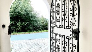 An arched doorway with a wrought iron gate leading to a paved area with a view of a road and greenery. - Schönblick B8 House · Mountain Charm with a View of Nature (Schöfweg)