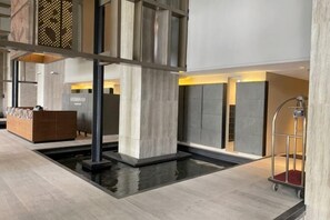 Un moderno vestíbulo de hotel con un mostrador de recepción, un elemento decorativo de agua y un carrito de equipaje.