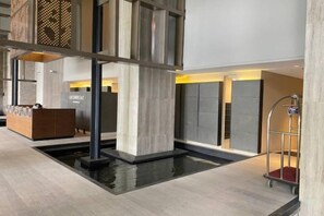 A modern hotel lobby with a reception desk, a water feature, and a luggage cart. - Bukit Bintang Lalaport Designer Studio KLCC View (Kuala Lumpur)