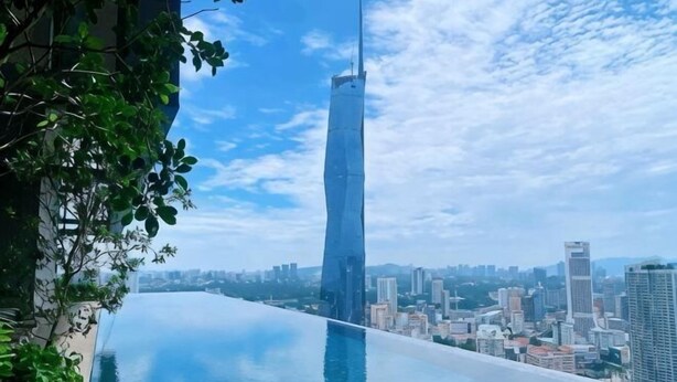 Una piscina que se extiende desde un edificio, con un paisaje urbano de fondo.