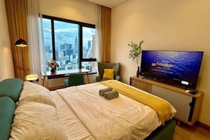 Habitació d'hotel amb un llit, televisió, finestra que mostra una vista de la ciutat i escriptori amb una làmpada.