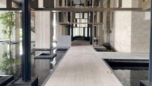 Interior moderno de un hotel con un corredor central, elementos acuáticos reflectantes y un techo alto con vigas estructurales.