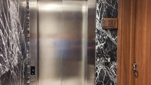 An elevator with a metallic interior and a marble wall with a number sign indicating the floor. - Jinhui Hotel (Casablanca)