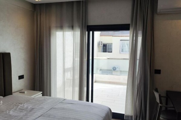 Une chambre d’hôtel comprenant un lit, une petite table de chevet, une chaise et une porte-fenêtre coulissante donnant sur un espace extérieur.