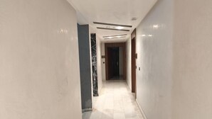 A hallway with a marble floor, white walls, and a wooden door at the end. - Jinhui Hotel (Casablanca)