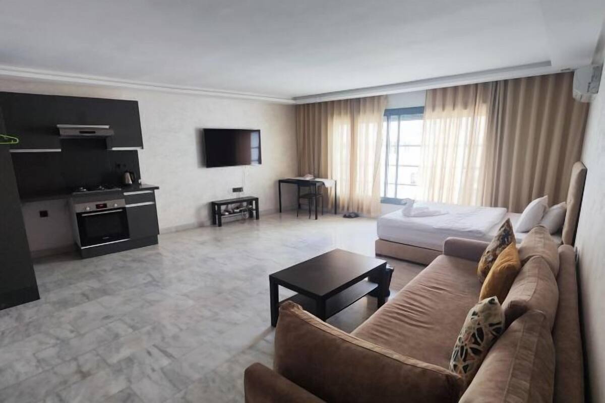 Una habitación de hotel moderna con sofá, una mesita, televisión, cama y kitchenette.