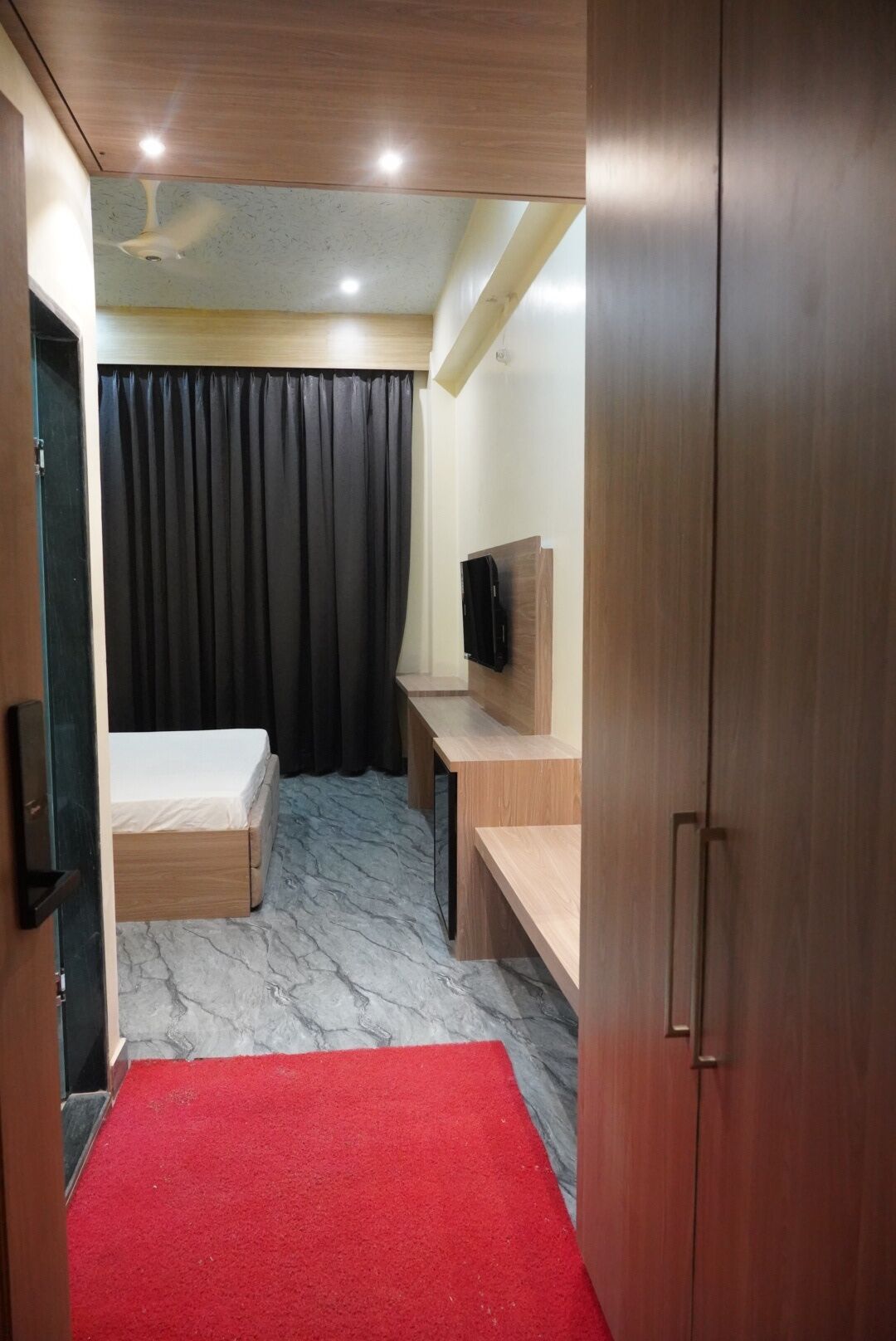 Une chambre d’hôtel de taille réduite, comprenant un lit, un bureau, une télévision et une moquette rouge.