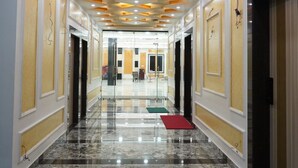 Ein Hotelgang mit poliertem Marmorboden, eingelassener Beleuchtung und einem symmetrischen Design, wobei auf beiden Seiten Türen angebracht sind.