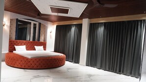 Ein modernes Schlafzimmer mit einem runden, gepolsterten Bett, einem Deckenventilator und einem großen Fenster mit Vorhängen.