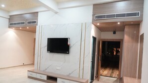 Ein modernes Wohnzimmer mit einem Flachbildfernseher an einer Marmorwand, Holzböden und eingebauten Stauraumelementen.
