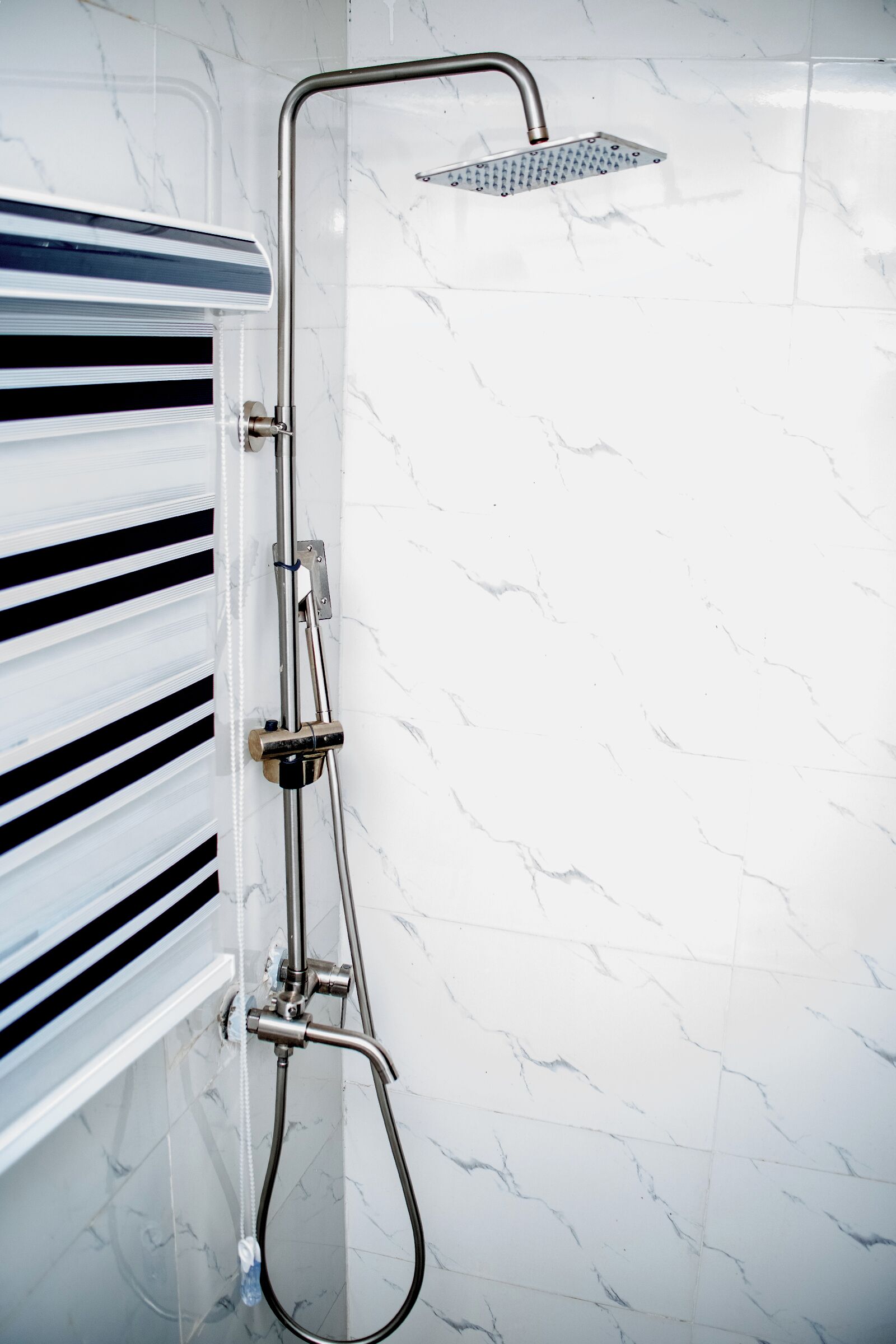 A modern shower with a handheld showerhead and a fixed showerhead, mounted on a wall with a marble-like pattern.