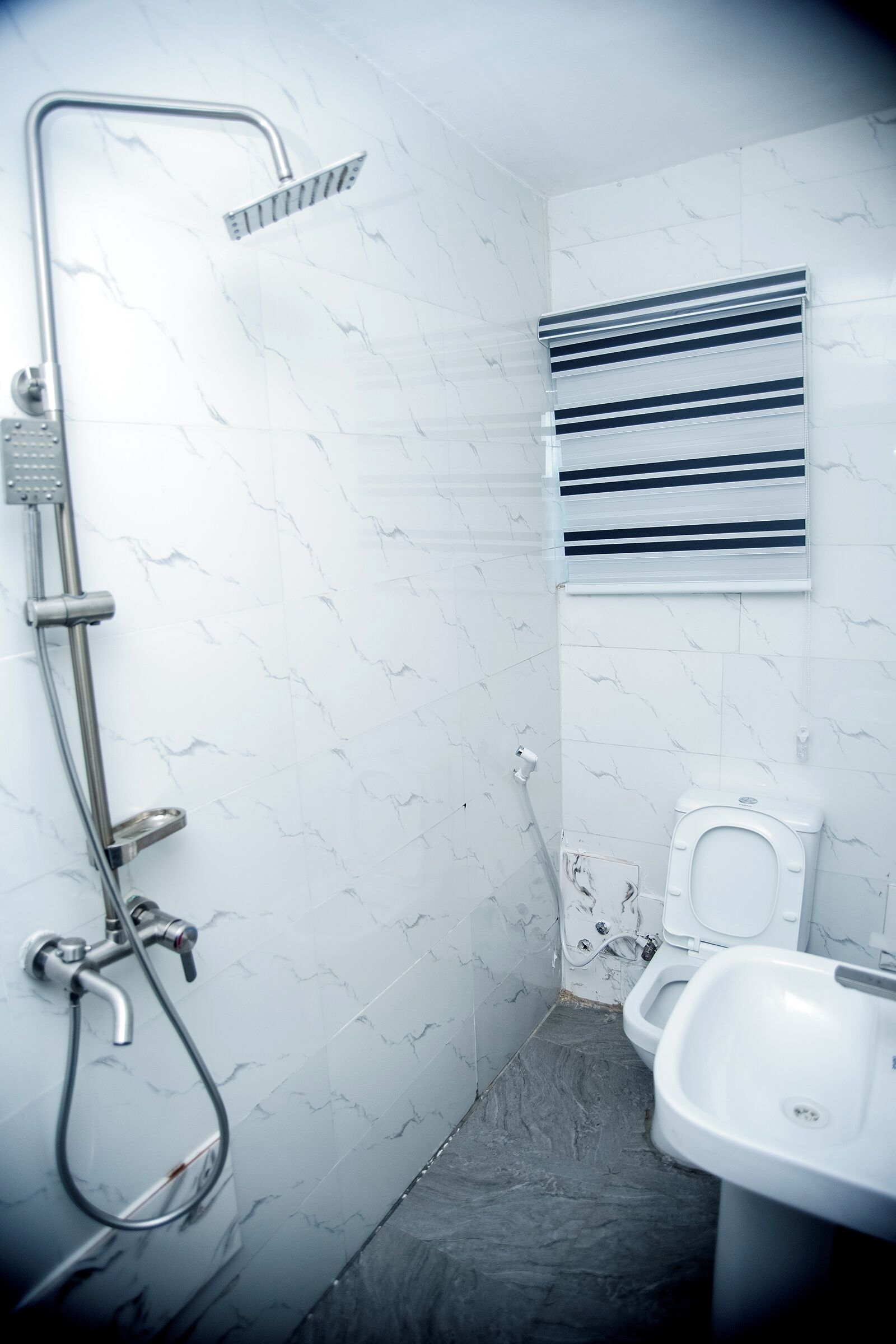 A bathroom with a shower, toilet, and sink, featuring white marble walls and a dark floor.