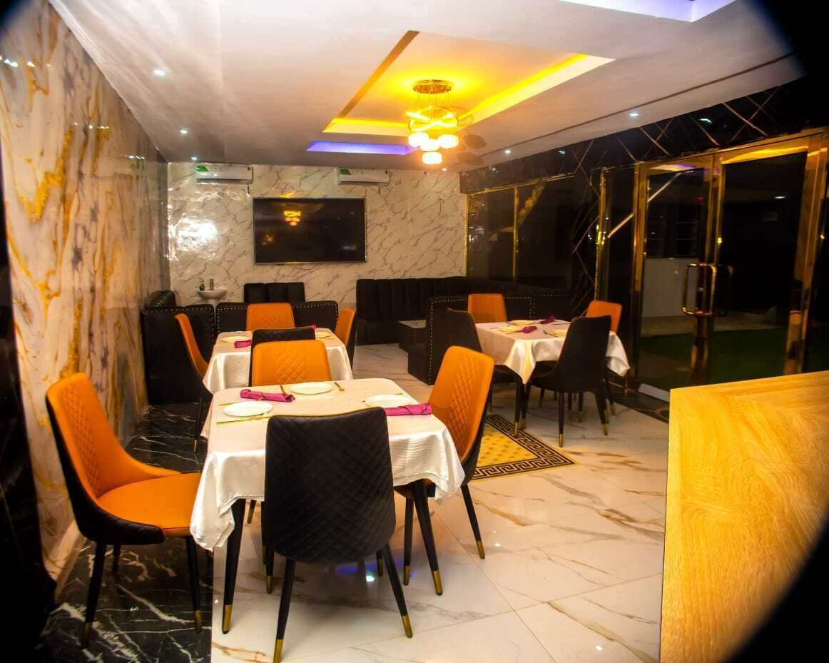 Un restaurante con paredes de mármol y sillas negras y anaranjadas. Las mesas están preparadas con manteles blancos y servilletas rosas.