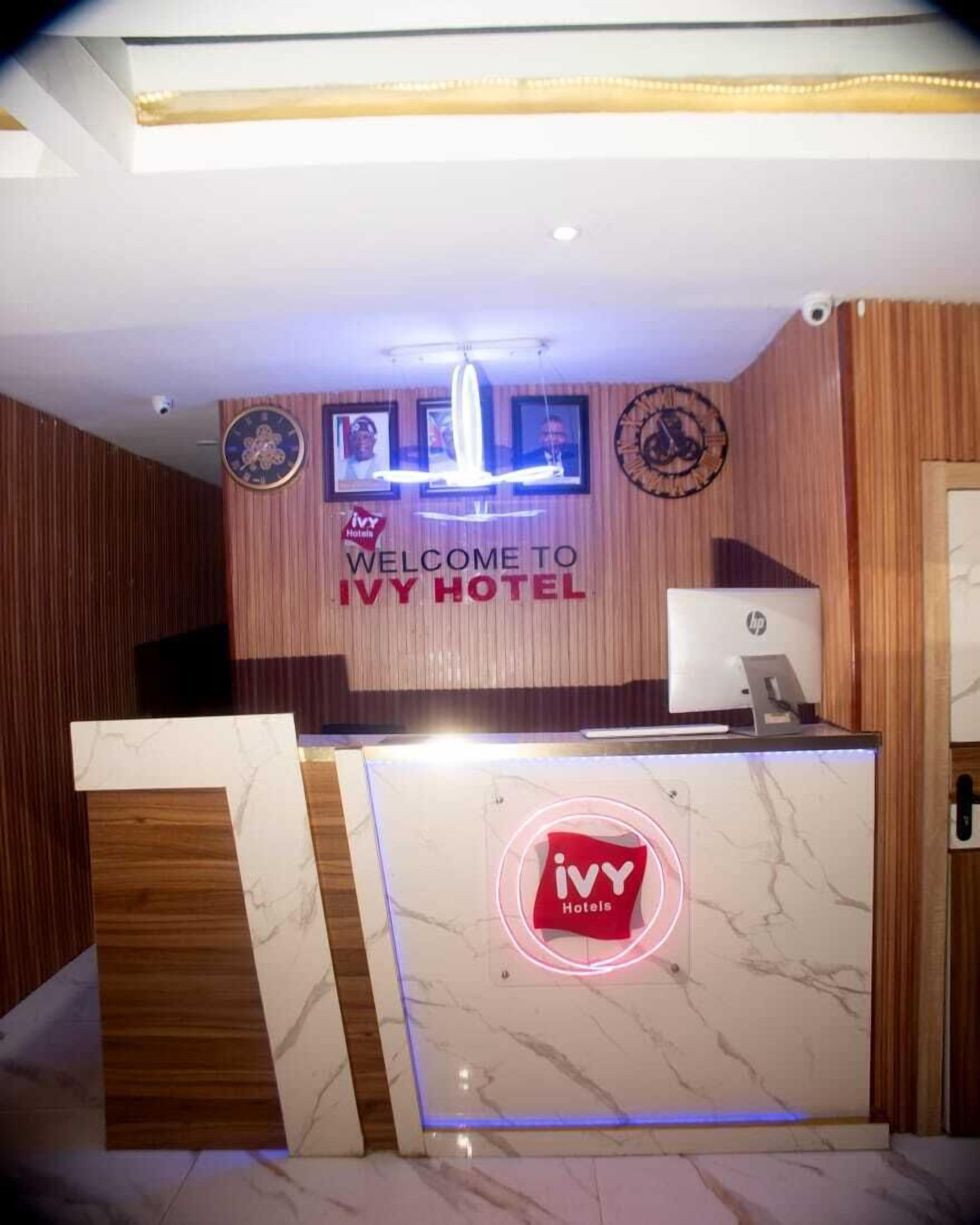 A hotel reception desk with a marble counter, a digital clock, and a sign that reads "WELCOME TO IVY HOTEL".