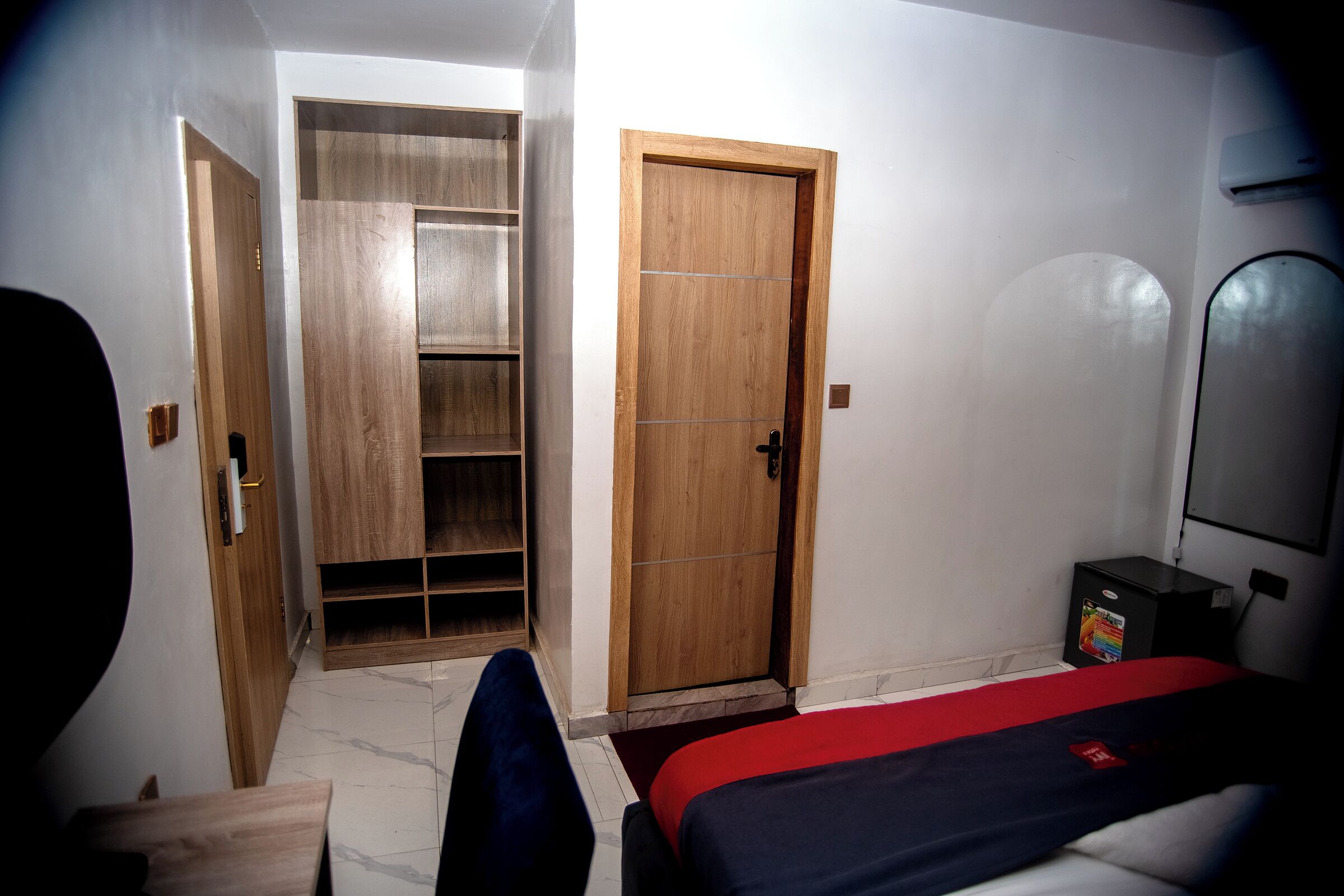 A room with a bed, a wardrobe, and a small desk with an air conditioner.