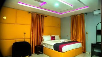 A modern hotel room with a large bed, orange curtains, and a bright ceiling with LED lighting.
