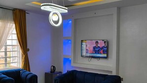 A modern living room with two sofas, a TV mounted on the wall, and a ceiling light fixture. - Ivy Hotel Epe (Epe)