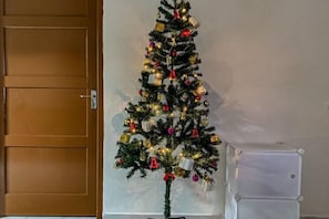 Ein Weihnachtsbaum mit Schmuck und Lichtern, eine Holztür und ein weißes Gerät im Hintergrund.