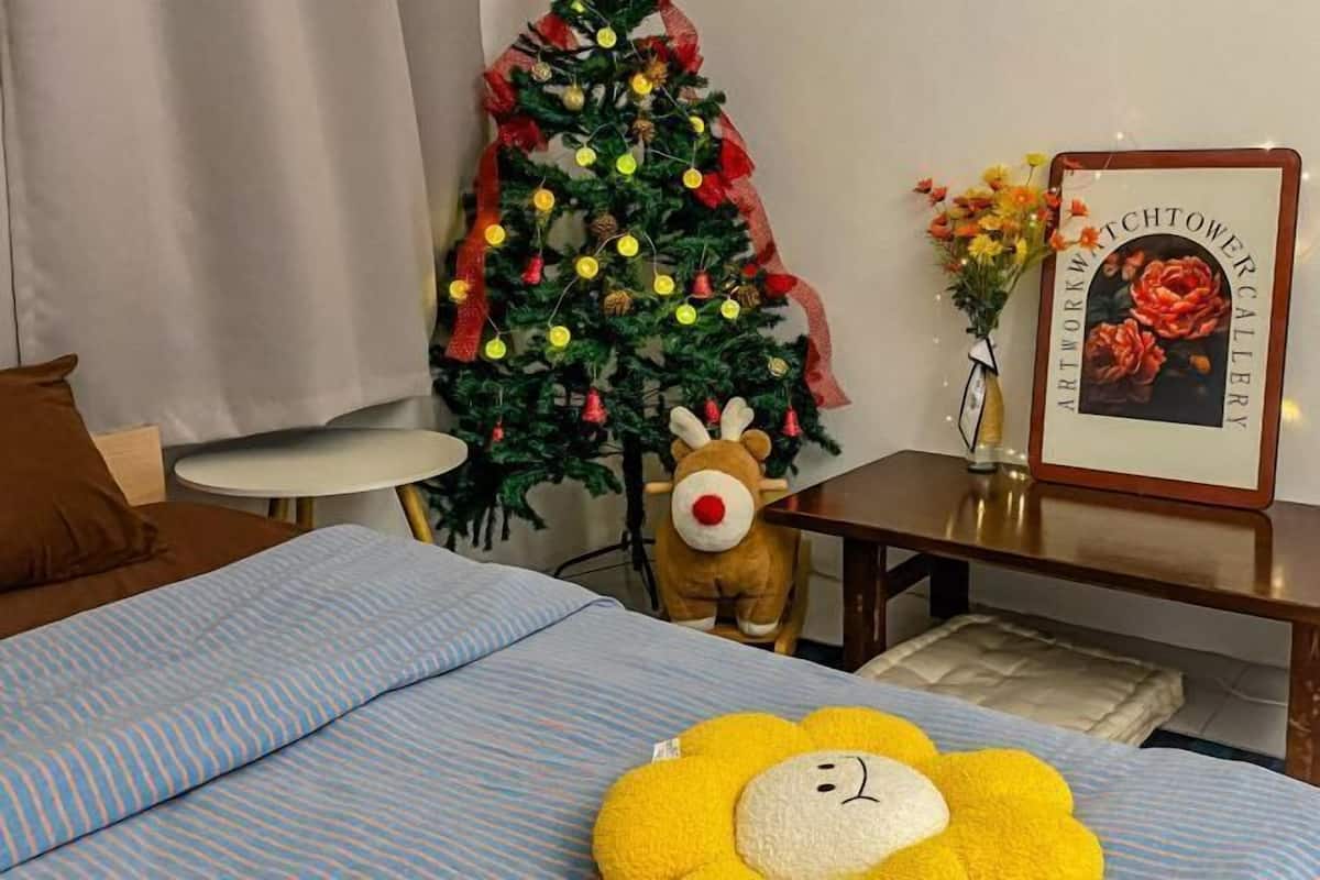 Un dormitori amb un llit, una taula petita, un arbre de Nadal, un quadre amb marc i un joguet de peluix.