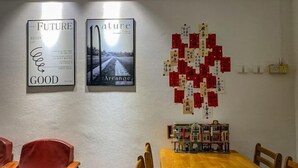 Un coin repas avec une table et des chaises en bois, deux affiches encadrées au mur et une petite bibliothèque remplie de livres.