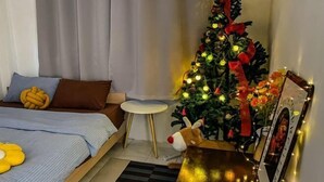Une chambre à coucher avec un lit, une petite table ronde, un sapin de Noël et un tableau encadré.