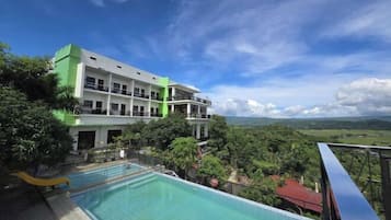 Un hotel con piscina, rodeado de exuberante vegetación y vistas a colinas distantes.
