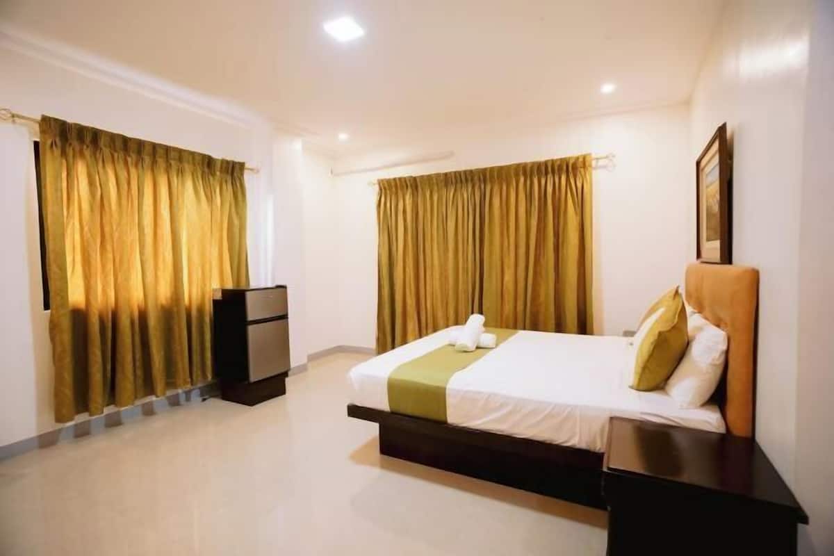 Una habitación de hotel con cama, mesita de noche, cómoda y cortinas.