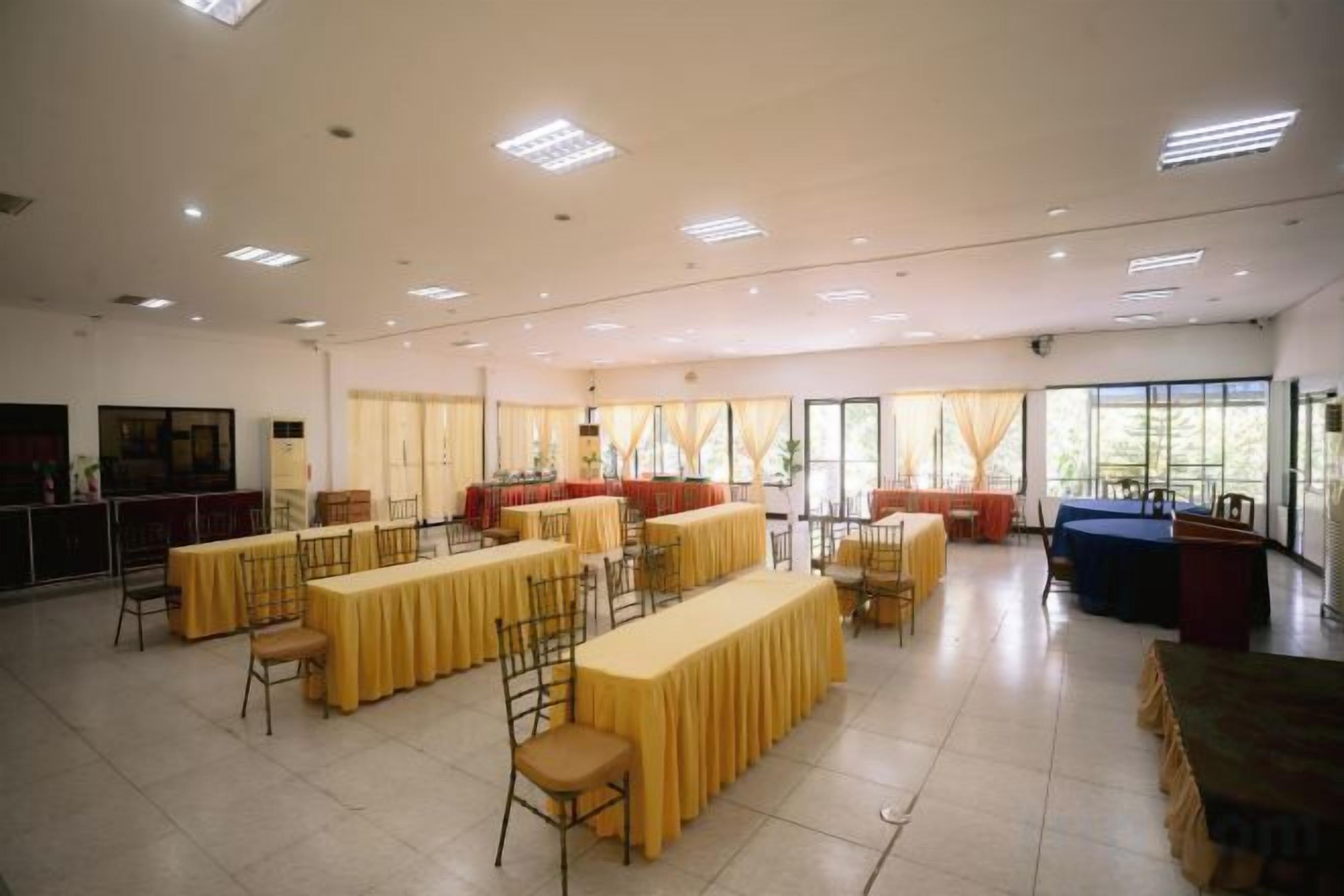 A spacious hall with multiple tables and chairs, large windows, and a high ceiling.
