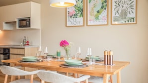 Un comedor con una mesa de madera dispuesta para cuatro personas, rodeada de sillas blancas. En la pared sobre la mesa hay impresiones enmarcadas de motivos botánicos.