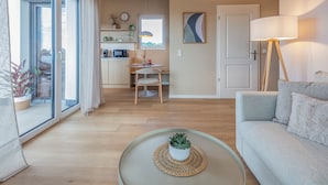 Una sala moderna con un sofá, una mesa redonda de centro con una planta, un comedor con mesa y sillas, y una cocina al fondo.