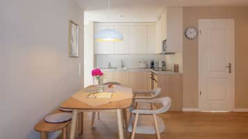 A modern kitchen with a wooden dining table, chairs, and a hanging light fixture.