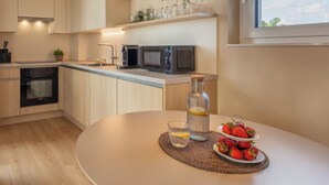 Una cocina moderna con una mesa de comedor redonda, horno empotrado, microondas y una estantería con cristalería y tazas.
