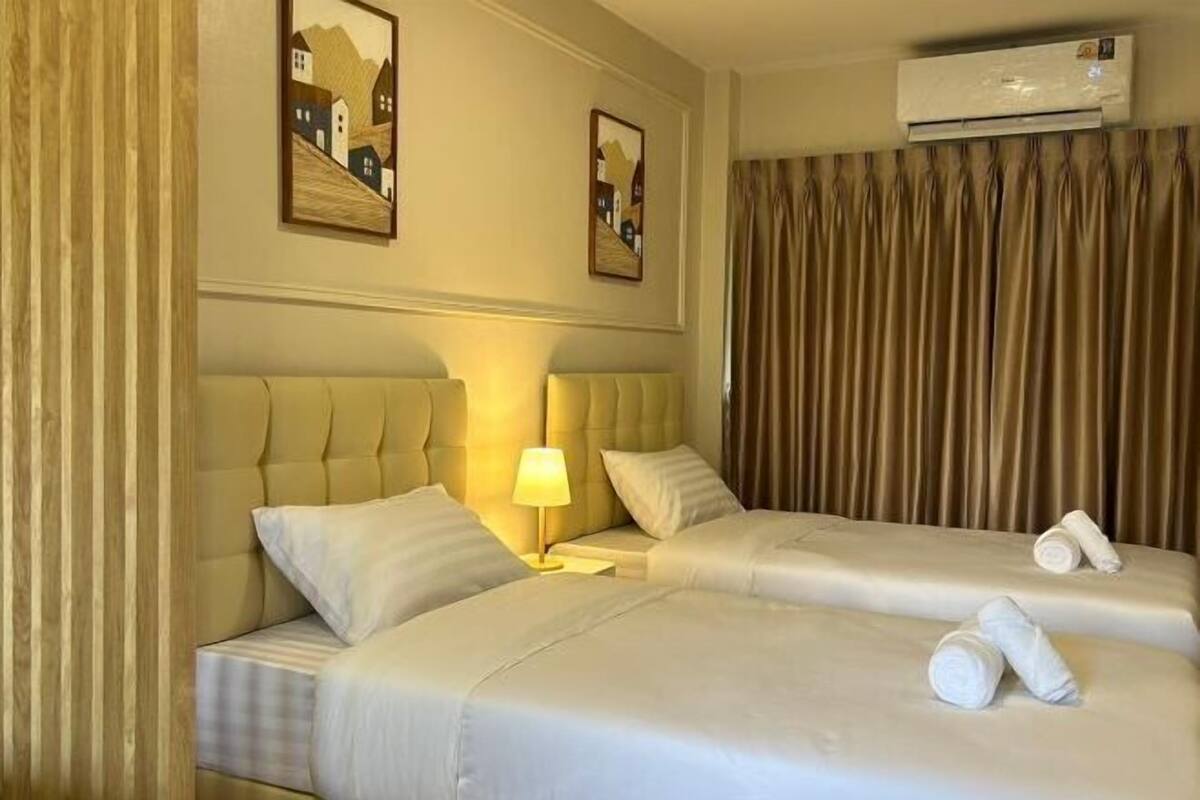 A hotel room with two beds, a headboard, a lamp, and a wall-mounted air conditioner.