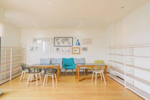 A room with a wooden floor, a sofa, a dining table with chairs, and shelves along the walls.