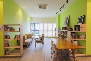 A room with a wooden table, chairs, a sofa, and bookshelves against green walls.