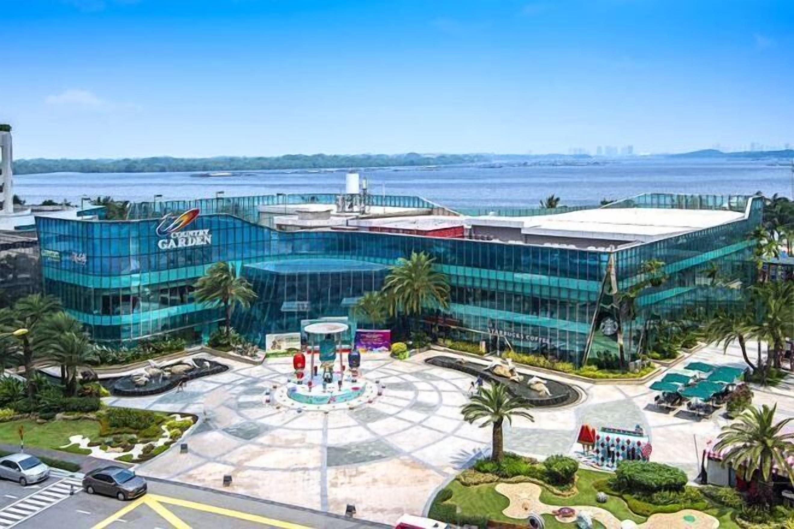 A modern building with a glass facade, a central courtyard with a fountain, and a view of the water body in the background.