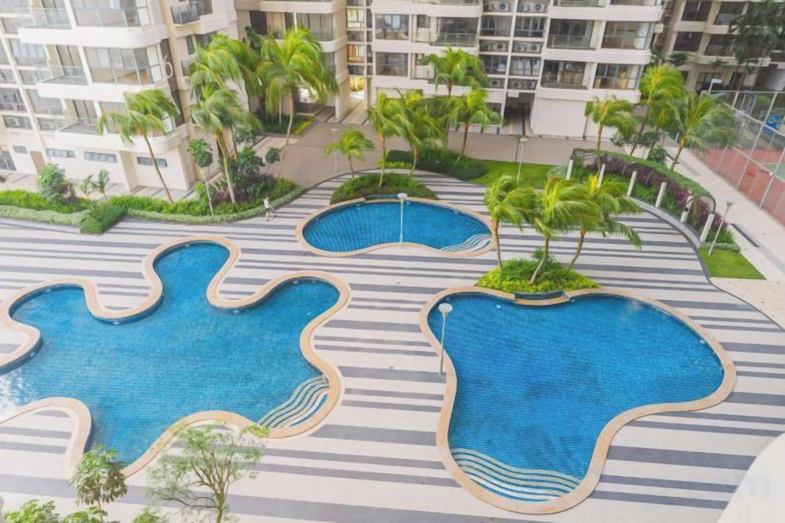A rooftop pool area with multiple irregularly shaped pools surrounded by palm trees and a landscaped garden.