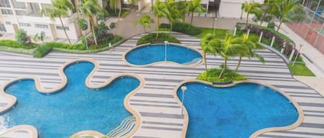 A rooftop pool area with multiple irregularly shaped pools surrounded by palm trees and a landscaped garden.