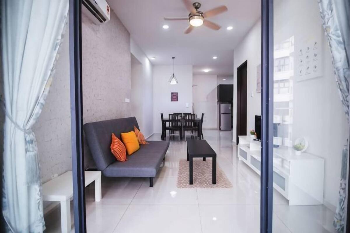 A modern living room with a sofa, a coffee table, a dining table, and a kitchen in the background.