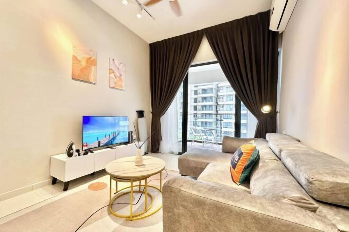 A modern living room with a sofa, a TV, a small table, and a view of a building through large windows.