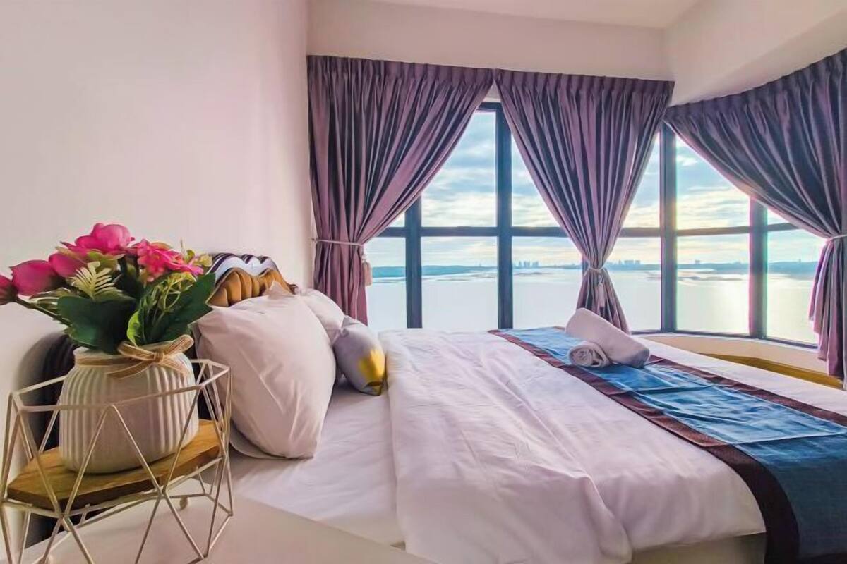 A hotel room with a bed, a view of the water, and curtains.