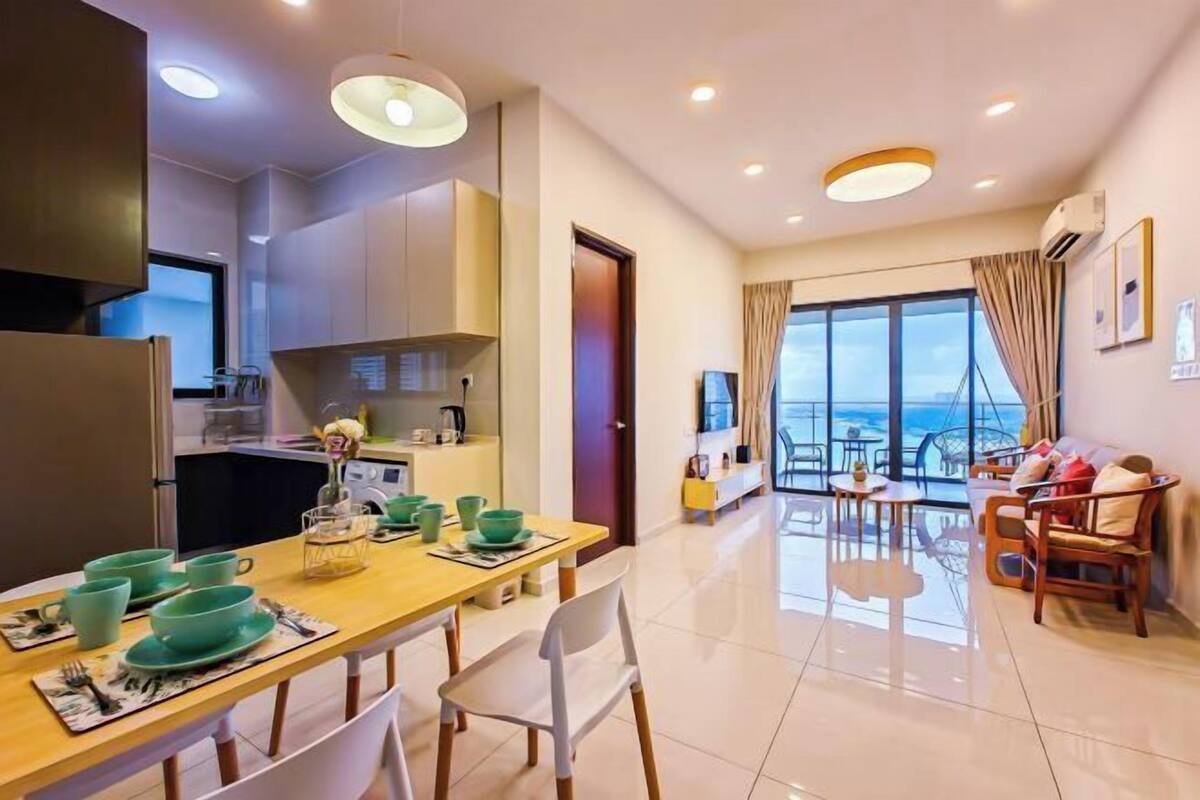 A modern hotel room with a dining area, kitchen, and a balcony with a city view.