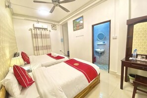 Une chambre d’hôtel avec deux lits, un bureau, une chaise, un ventilateur de plafond, une salle de bain avec un lavabo et une porte donnant sur un espace extérieur.