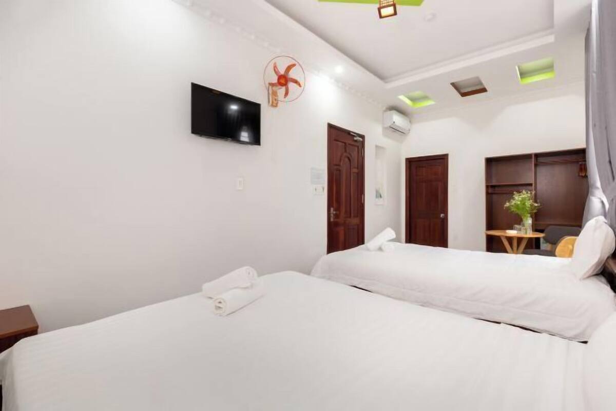 Une chambre d’hôtel avec deux lits, un téléviseur à écran plat, un ventilateur de plafond et une petite table agrémentée d’une plante.