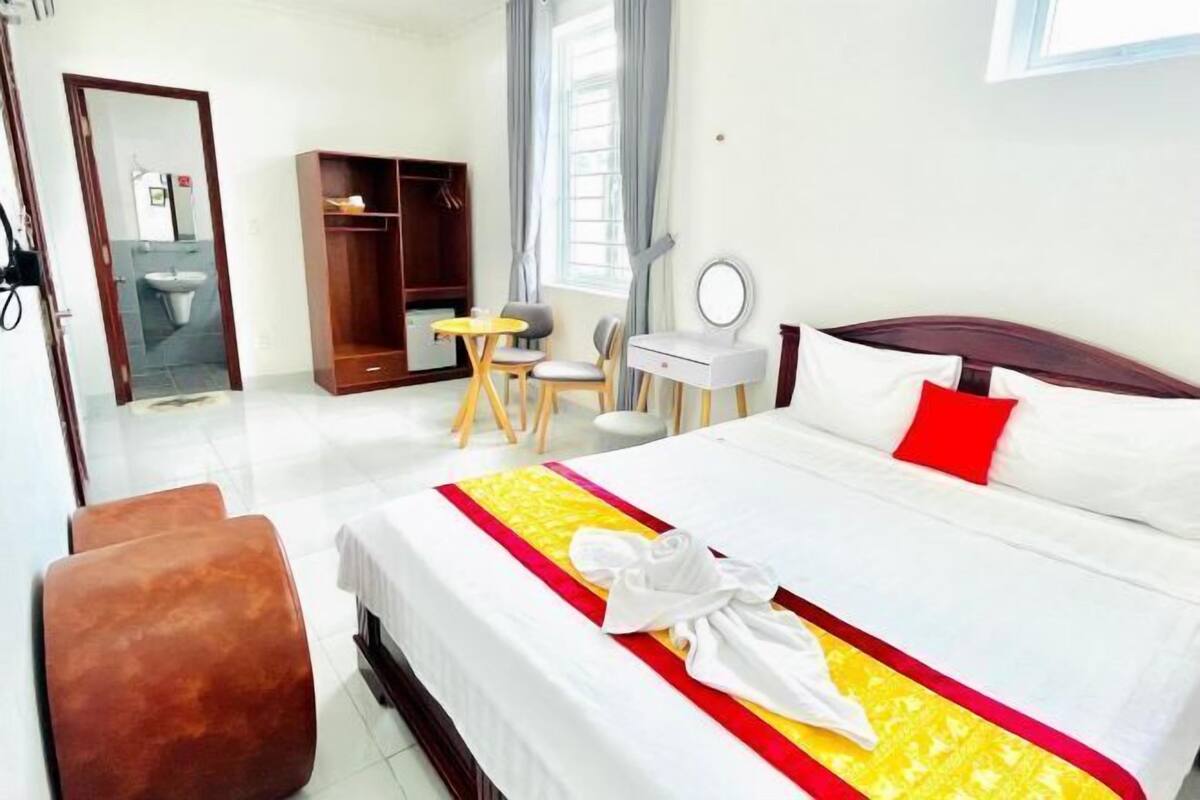 Une chambre d’hôtel comprenant un lit, un bureau, une chaise, une armoire et une salle de bain visible à travers une porte ouverte.