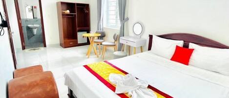 Een hotelkamer met een bed, een bureau, een stoel, een kledingkast en een badkamer die door een open deur zichtbaar is.