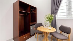 A room with a wooden wardrobe, a small refrigerator, a round wooden table with two chairs, and a window with curtains. - Luxury Vuon Lai Hotel (Ho Chi Minh City)