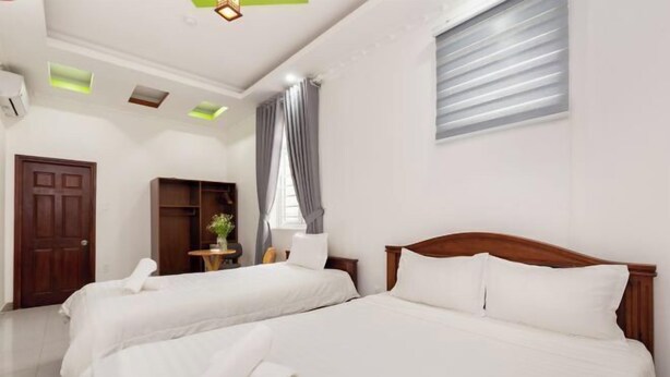 A hotel room with two beds, a wooden door, a small table with a plant, and a window with curtains. - Luxury Vuon Lai Hotel (Ho Chi Minh City)