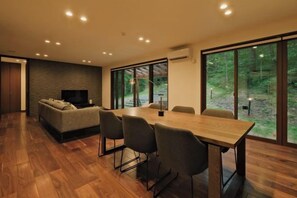 A modern dining area with a wooden table and chairs, a sofa, and a television. - Fandina Fujiwara (Tsumagoi)
