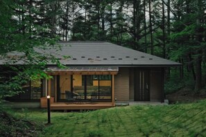 A modern house with a large glass window, a wooden deck, and a forested backdrop. - Fandina Fujiwara (Tsumagoi)